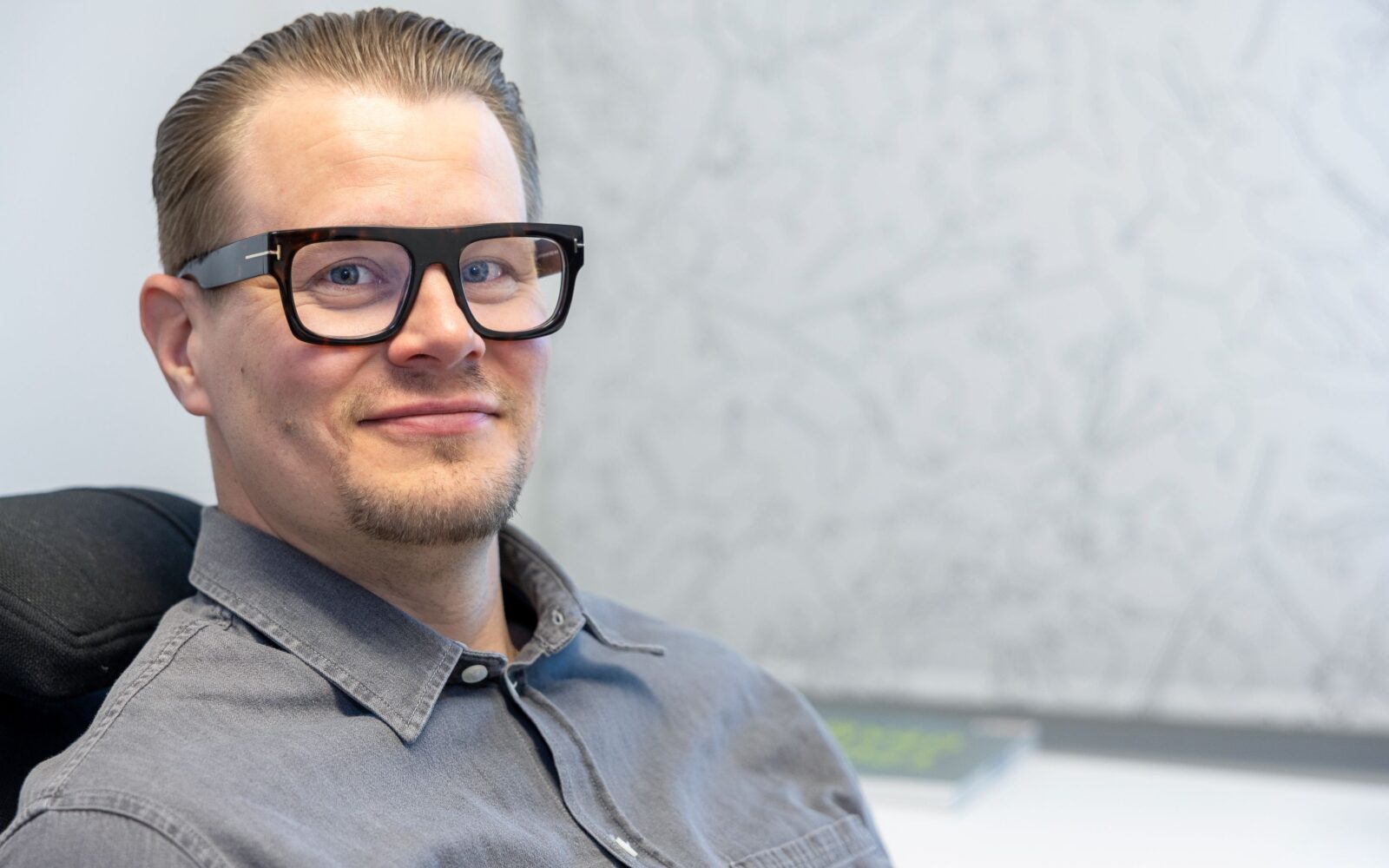 Mies harmaassa paidassa on lähikuvassa ja istuu.