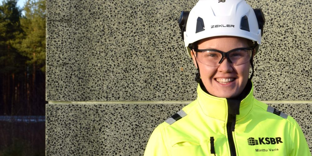 Hymyilevä rakennustyöntekijä seisoo betoniperustuksen edessä.