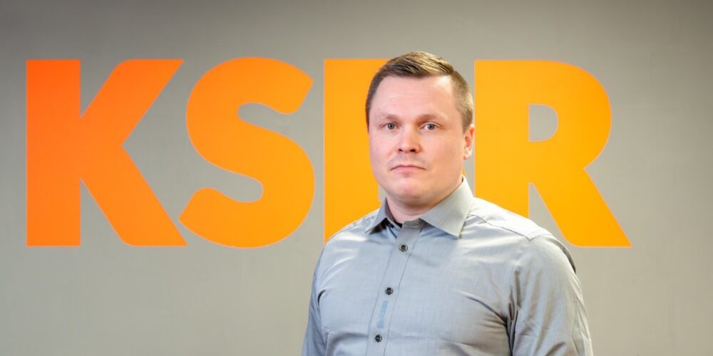Toimitusjohtaja seisoo KSBR:n logoseinän edessä.