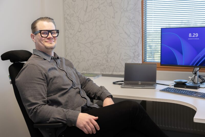 Mies harmaassa paidassa istuu työpöydän ääressä.