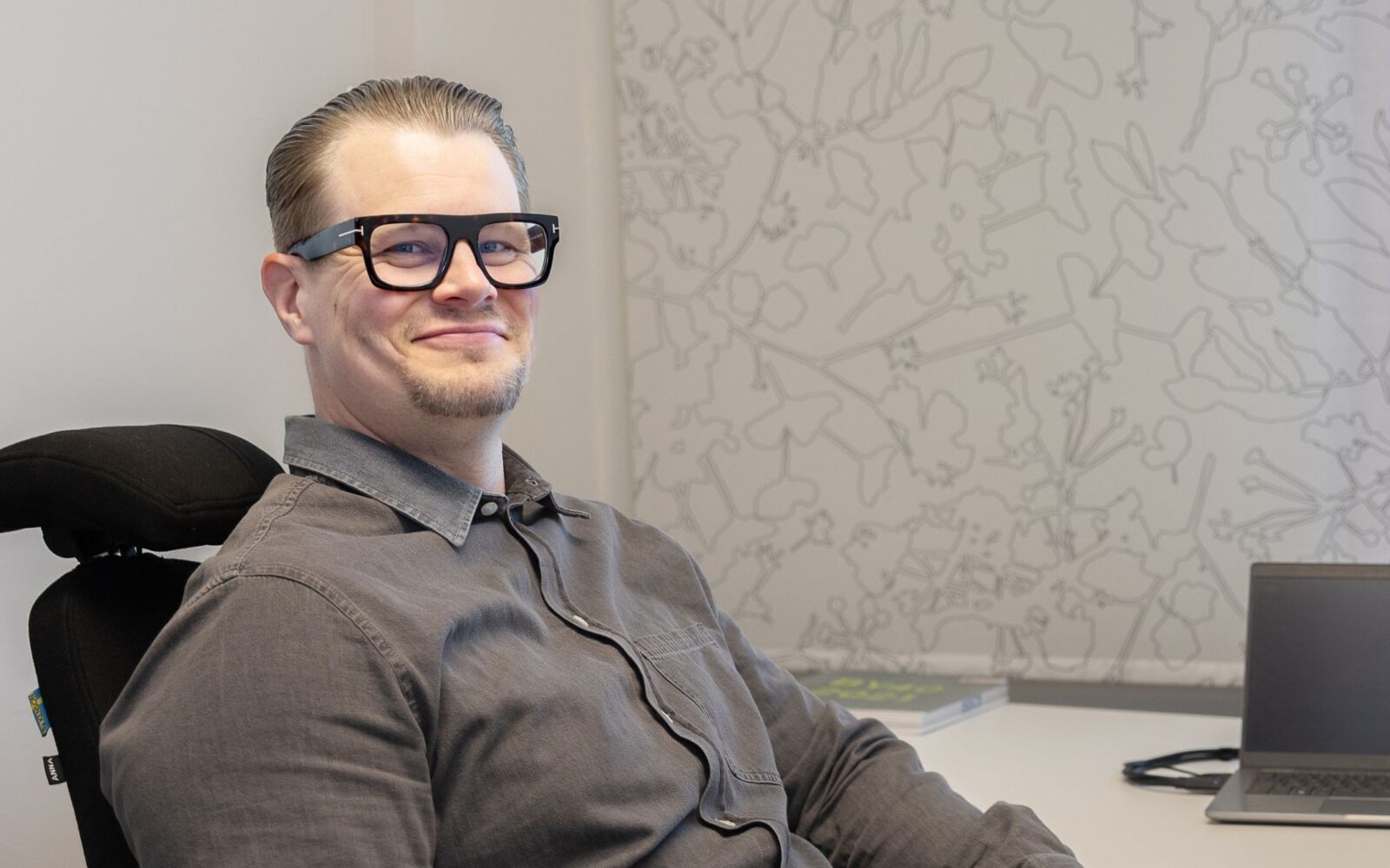 Mies harmaassa paidassa istuu tietokoneen ääressä.