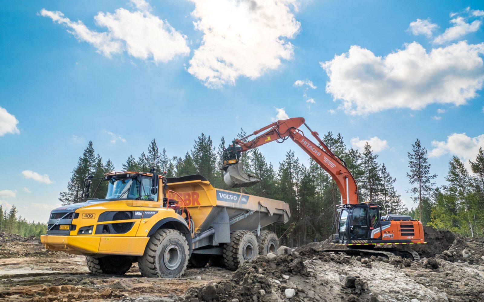 Maansiirtokone kaivaa maata aurinkoisessa säässä metsäisellä alueella.